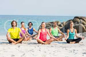 Friends meditating in lotus position on shore at beach
