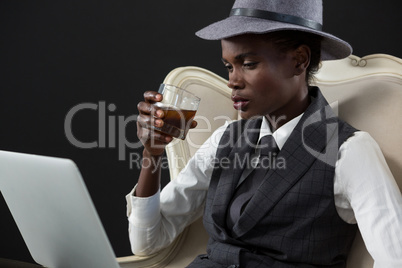 Androgynous man drinking whiskey while sitting on a chair