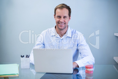 Portrait of smiling dentist working on laptop