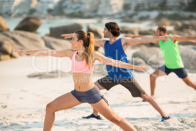 Friends practicing warrior pose on shore