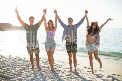 Friends holding hands with arms raised on shore at beach