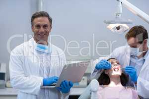 Portrait of dentist holding laptop at dental clinic