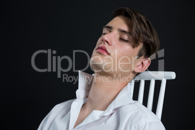 Androgynous man posing while sitting on chair with eyes closed