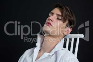 Androgynous man posing while sitting on chair with eyes closed