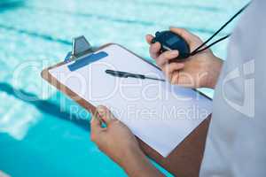 Swim coach looking at stopwatch at poolside