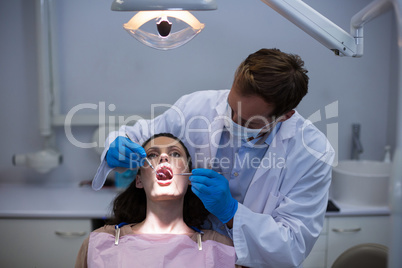 Dentist examining a female patient with tools