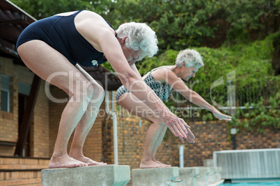 Two senior women preparing to dive in pool