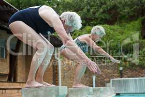 Two senior women preparing to dive in pool