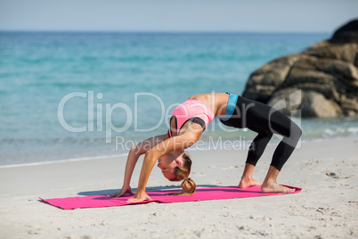 Side view of young woman exercising on exercise mat at beach