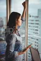 Side view of woman holding tablet while looking through window