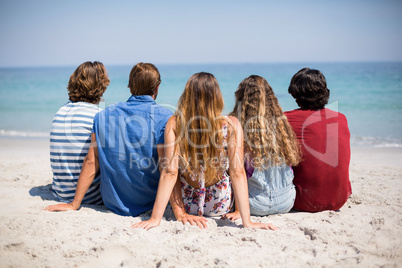 Friends sitting on shore at beach during sunny day