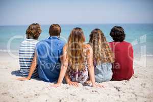 Friends sitting on shore at beach during sunny day