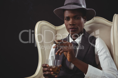 Androgynous man holding cigar while while sitting on a chair