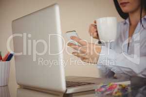 Close up of woman using smart phone while sitting by laptop