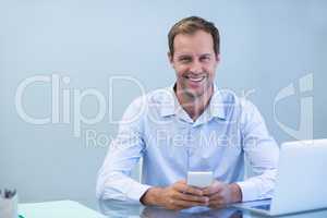 Smiling doctor using mobile phone in dental clinic