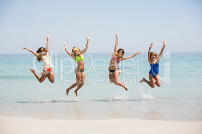 Friends in bikinis jumping on shore