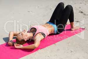 Young woman lying down on exercise mat at beach