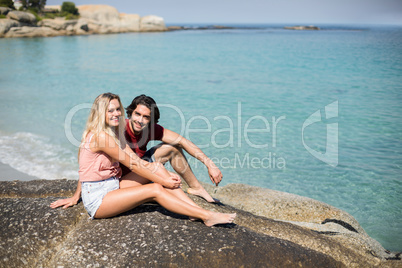 Portrait of happy couple sitting on rock by sea