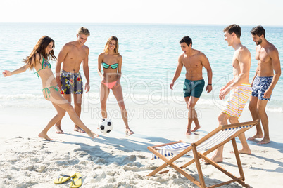 Happy friends playing soccer on shore at beach