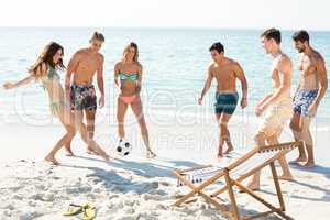 Happy friends playing soccer on shore at beach