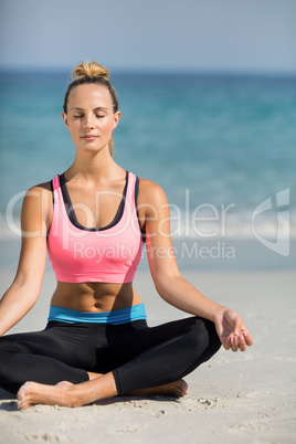 Beautiful woman meditating in lotus position at beach