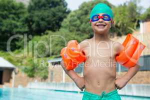 Boy wearing arm bands standing at poolside