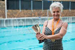 Senior woman holding trophy at poolside