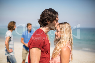 Man kissing girlfriend on forehead against friends at beach