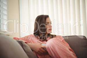 Woman looking away while sitting on sofa against curtains