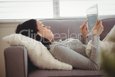 Side view of woman using tablet while lying on sofa