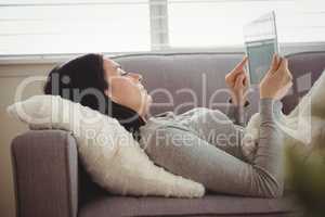 Side view of woman using tablet while lying on sofa