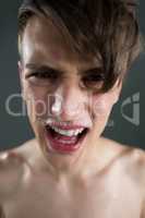 Shirtless androgynous man crying against grey background