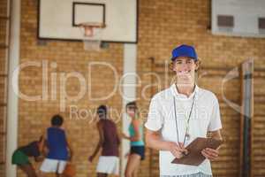 Coach smiling at camera while high school team playing basketball in background