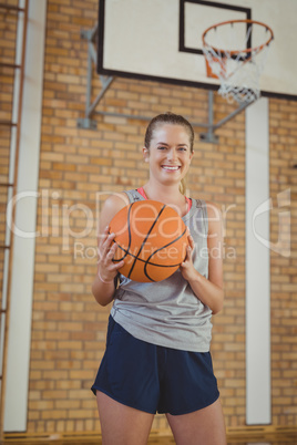 Smiling high school girl holding a basket ball in the court