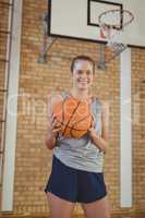 Smiling high school girl holding a basket ball in the court