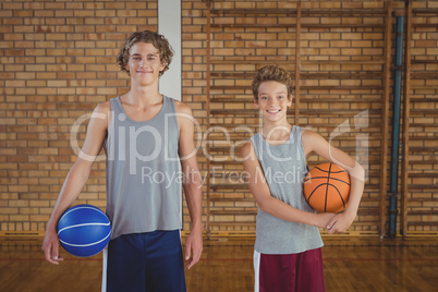 Smiling high school boys holding basketball in the court
