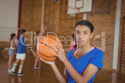 High school girl holding a basketball while team playing in background