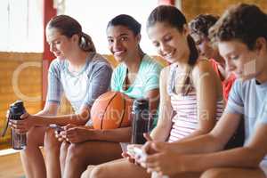 High school kids using mobile phone while relaxing in basketball court