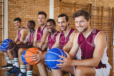 Smiling basketball players sitting on bench with basketball in the court