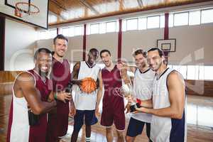 Smiling basketball players standing with throphy in the court