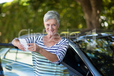 Senior woman holding phone while leaning on car door