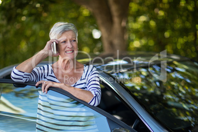 Senior woman talking on phone by car