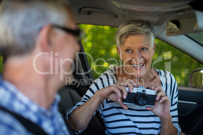 Senior woman photographing man in car