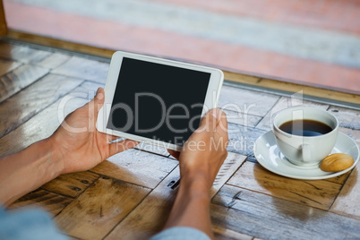 Cropped image of man holding tablet computer by coffee cup