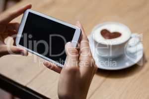 Woman photographing coffee cup on table at sidewalk cafe