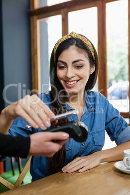 Woman making payment on credit card reader at cafe shop