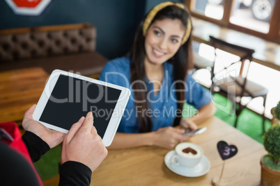 Cropped image of owner holding tablet while customer sitting at table