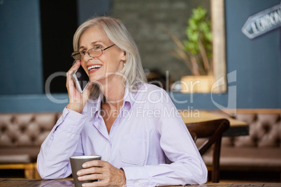 Senior woman talking on smart phone while holding mug at cafe