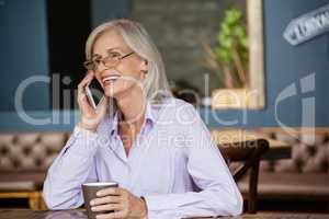 Senior woman talking on smart phone while holding mug at cafe