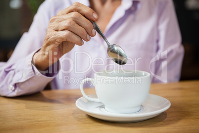 Woman stirring coffee while sitting at table in cafe